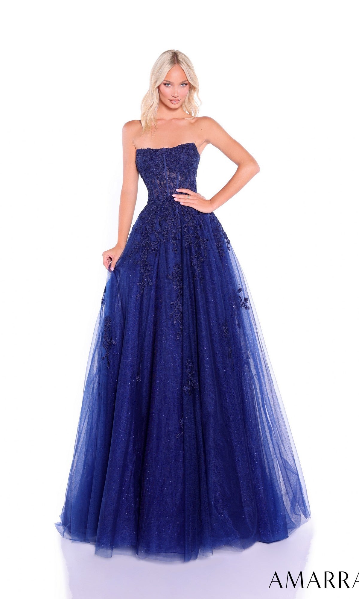A woman poses against a white background in the Amarra 88950 Strapless Embroidered Prom Ball Gown—a dark blue, floor-length A-line dress with a sweetheart neckline and exquisite floral embroidery.